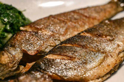 Pastrmka sa roštilja servirana na tanjiru u restoranu. Ukusna riba servirana sa krompirom i špinatom. Ukusna pečena riba pripremljena za večeru.