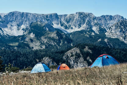 Kampovanje u prirodi. Rasklopljeni šatori sa pogledom na vrhove planina. Prijevor.