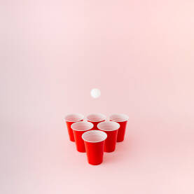 Šest crvenih plastičnih čaša za beer pong igru s bijelom lopticom koja lebdi iznad.