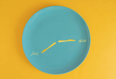 Tanjir tirkiznoplave boje na jarkožutoj podlozi sa žutim nožem i viljuškom kao kazaljkama sata na kojemu arapskim slovima piše: sehur - ramazanski doručak i iftar - ramazanska večera.