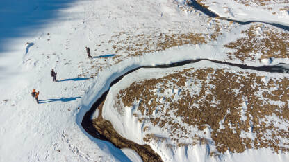 Tri planinara šetaju pored Studenog potoka na Bjelašnici u blizini sela Umoljani. Zimske aktivnosti na otvorenom, planinarenje na snijegu, priroda, uživanje. Aerial photo, fotografija dronom.