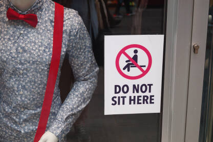 Zabranjeno sjedenje. Do not sit here. Izlog sa znakom zabranjeno sjedenje ispred prodavnice.