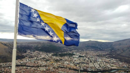 Državna zastava Bosne i Hercegovine se vijori na vjetru. Nacionalna zastava Bosne i Hercegovine na jarbol iznad grada Mostara, snimak dronom.
