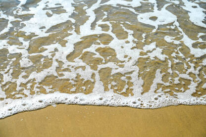 Morski valovi s pjenom na pješčanoj plaži. Pijesak na plaži.