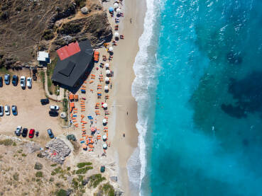 Snimak dronom mora i egzotične plaže ljeti. Suncobrani i ležaljke na plaži. Morski talasi. Turizam i putovanja.