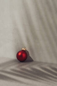 Crvena božična kuglica, ukras na betonskoj pozadini sa sjenom palminog lista.