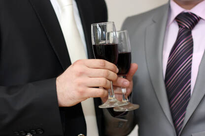 Nazdravljanje sa vinom Dva muškarca u odijelima nazdravljaju sa čašama u kojima se nalazi vino