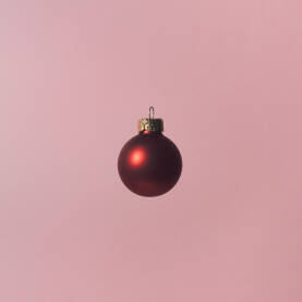 Crvena božićna kuglica / ukras levitira na ružičastoj pozadini.Božićna / Novogodišnja čestitka.