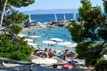 Makarska, Hrvatska: Turisti na plaži i u moru. Ljetni godišnji odmori. Obala Jadraskog mora ljeti. Turistička sezona. Ljudi se sunčaju i kupaju.