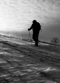 Planinar u usponu ka vrhu brda na snijegu i vjetru, crno-bijelo.