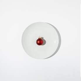 Ukrasna crvena kuglica na bijelom tanjuru. Božićna, Novogodišnja čestitka.