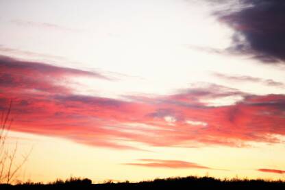 Zalazak sunca koji pusta prelepe boje gde su oblaci crvenii ljubicasti, u donjem delu fotografije crno polje