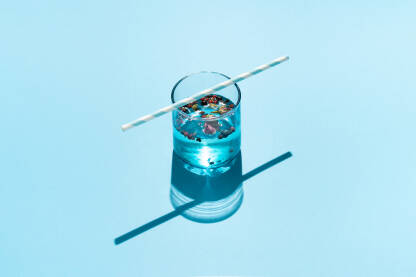 Piće u plavoj staklenoj čaši sa začinima i papirnom slamkom na plavoj pozadini.
