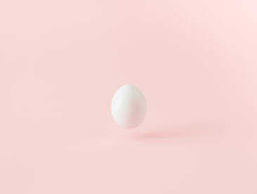 Bijelo jaje lebdi u zraku na ružičastoj pozadini.