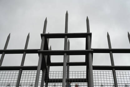 Šiljci ograde uzdižu se prema olujnim oblacima. Vrh metalne ograde naspram tamnog dramatičnog neba. Oštra metalna ograda pod teškim tamnim oblacima.