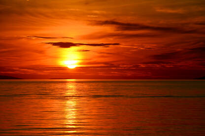 Prekrasan narančasti zalazak sunca na moru. Sunce zalazi za horizont. Mirni valovi na moru.