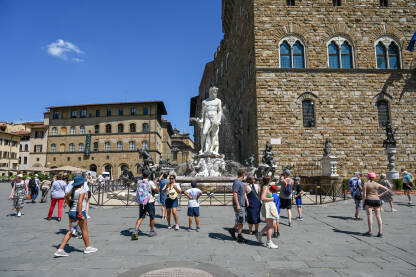 Firenze, Italija: Turisti istražuju grad. Neptunova fontana na Piazza della Signoria. Ljudi šetaju trgom. Zgrade u centru grada.