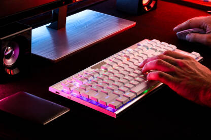 Osoba kuca na tastaturi koja se nalazi na radnom stolu izmedju monitora, miša,zvučnika i hard diska obasijana led svijetlima