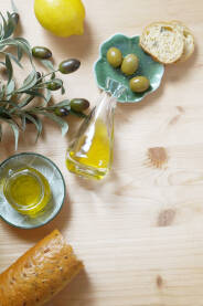Maslinovo ulje na stolu sa maslinama, limunom, maslinovom granom i baguette-om
