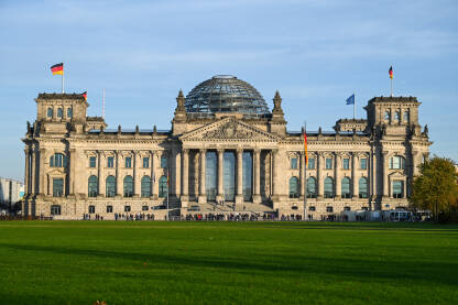 Berlin, zgrada njemačkog parlamenta. Njemačke nacionalne zastave se vijore na jarbolu ispred zgrade Reichstaga u Berlinu, Njemačka. Njemački Bundestag.