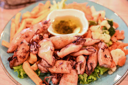 Lignje na žaru sa svježom salatom i krompirom servirani na tanjiru u restoranu. Zdrava morska hrana.