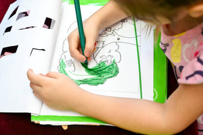 Djevojčica boji i crta bojicama po bloku papira. Djeca crtaju na stolu u školi. Obrazovanje djece.