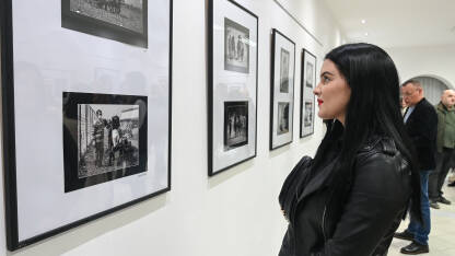 Djevojka gleda fotografije na izložbi. Izložba fotografija u zatvorenom prostoru. Posjetioci izložbe fotografija u galeriji.