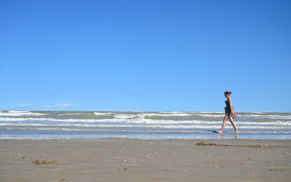 Žena šeta pješčanom plažom uz more ljeti. Turisti uživaju i zabavljaju se na plaži. Jadransko more, Lido di Jesolo, Italija.