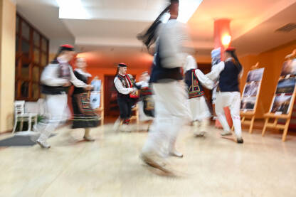 Zamućena fotografija grupe ljudi koji plešu. Muškarci i djevojke u tradicionalnoj narodnoj nošnji plešu. Tradicionalni ples. Kolo je južnoslovenski ples koji se izvodi na priredbama.