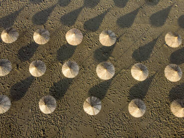 Suncobrani na pješčanoj plaži uz more, snimak dronom. Suncobrani od trstike na obali mora.