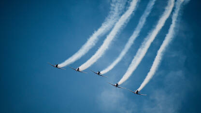 Avioni na plavom nebu tokom aeromitinga. Pet aviona u formaciji. Tim za prikaz zraka leti u zrakoplovima s dimnim tragovima.
