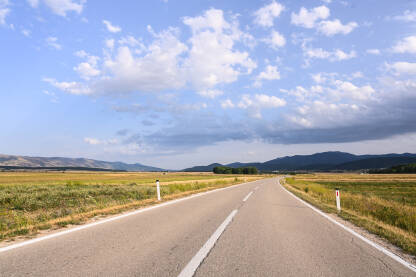 Cesta koja vodi kroz polje u predvečerje. Prazan asfaltni put. Saobraćaj. Pogled na cestu sa pozicije vozača u autu.