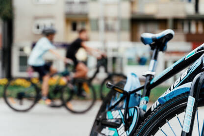 Biciklisti voze bicikle kroz gradske ulice, dok je u prvom planu parkiran bicikl, a pozadina zamagljena.