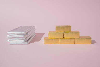 Čokoladni blokovi i ploče u srebrenom i zlatnom papiru na pastelnoj pink pozadini sa praznim prostorom. Zlatne i srebrene poluge, koncept.