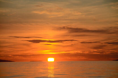 Prekrasan narančasti zalazak sunca na moru. Sunce zalazi za horizont. Mirni valovi na moru.