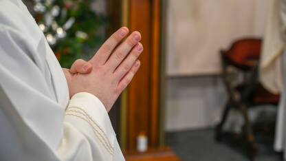 Katolički svećenici u liturgijskim odorama se mole sa sklopljenim rukama. Ruke čovjeka koji se moli u katedrali. Božićna misa polnoćka u crkvi.