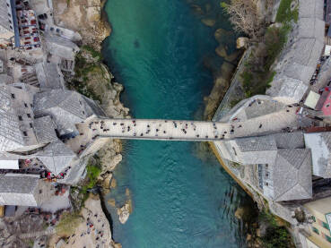 Stari most iznad rijeke Neretve u Mostaru, Bosna i Hercegovina. Ljudi prelaze Stari most, snimak dronom.