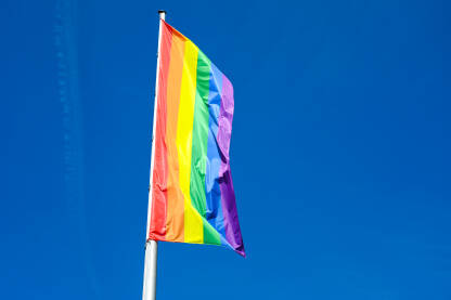 LGBTIQ zastava se vijori na vjetru na jarbolu u gradu. Simbol LGBT zajednice i društvenog pokreta. Simbol lezbejske, gej, biseksualne, transrodne i queer zajednice.