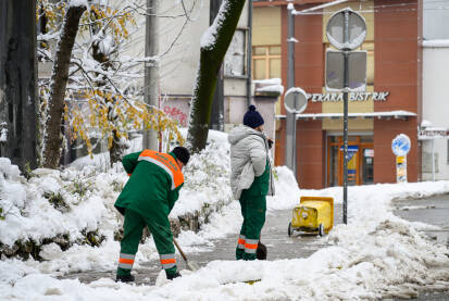 Radnici komunalnog preduzeća čiste snijeg sa trotoara tokom zimskog dana u Sarajevu. Prikaz svakodnevnog održavanja grada i zimskih uslova na ulicama.
