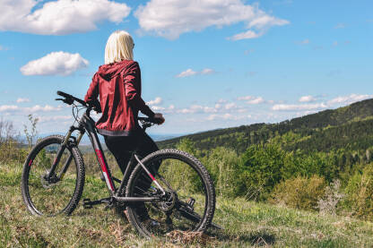 Biciklizam u prirodi. Djevojka naslonjena na bicikl sa pogledom na vrhove planina.