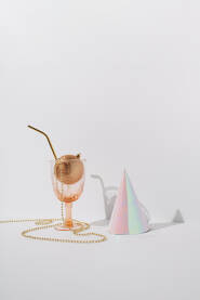 Čaša za piće sa zlatnom ukrasnom kuglicom, perlama i slamkom i papirnom kapom na bijeloj pozadini. Novogodišnja, božićna čestitka.