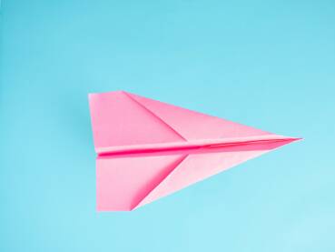 Papirni avion roze boje na svjetloplavoj podlozi, putovanje, letovi, koncept.