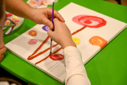 Dijete s autizmom ili razvojnim poteškoćama slika bojama na papiru tokom art terapije.