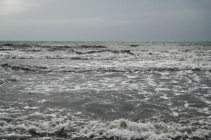 Olujno vrijeme na obali. Mutna morska voda nakon kiše. Valovi mora s pješčano smeđom i sivom bojom.