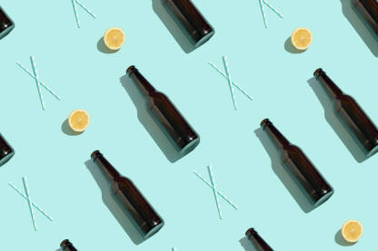 Staklene boce za pivo, limun i slamke na plavoj podlozi.