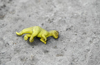Žuta plastična igračka dinosaura. Odbačena dječja igračka na podu.