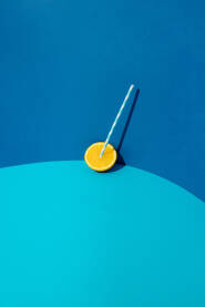 Pola svježe naranče s plastičnom plavo - bijelom slamkom za piće na plavoj pozadini. Ljetni koncept.