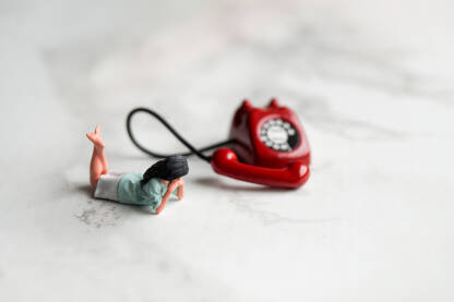 Mali crveni telefon na stolu sa podignutom slušalicom i figuricom djevojke.