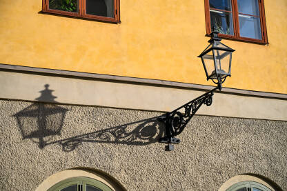 Ulična rasvjeta. Klasična ukrašena crna metalna vanjska zidna lampa s trokutastim nosačem u obliku spirale. Tradicionalna zidna lampa od lijevanog željeza s ukrasnim ornamentima i staklenim pločama.