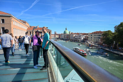 Venecija, Italija. Turisti fotografišu. Venecija, Italija. Turisti fotografišu. Historijske zgrade duž riječnog kanala. Čamci i gondole na rijeci. Popularna turistička destinacija.